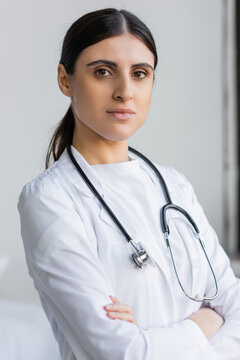 Portrait of brunette doctor crossing arms and looking at camera in hospital.