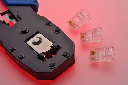 A rg45 connector for an internet cable and a twisted pair crimper lie on a multi-colored background. Close-up