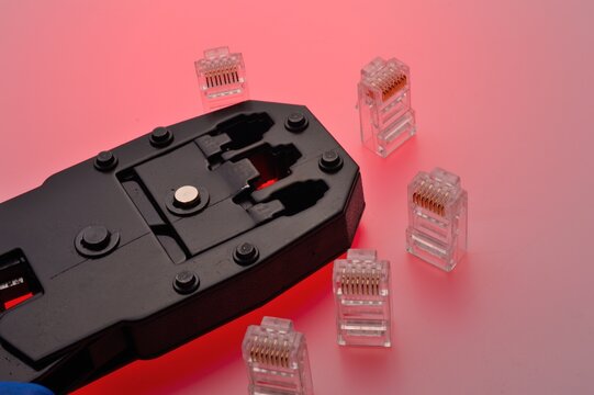 A rg45 connector for an internet cable and a twisted pair crimper lie on a multi-colored background. Close-up