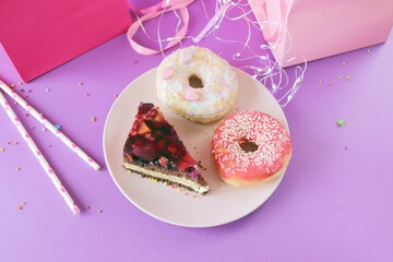 A piece of chocolate cake with cream and berries and sweet donuts on a plate, holiday gifts and...