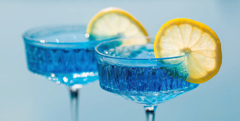 A glass of delicious blue cocktail Blue Lagoon and yellow lemons on the background of the pool. Alcoholic cocktail juicy fruit blue with curacao liqueur, ice cubes and a slice of lemon. © Юлия Клюева