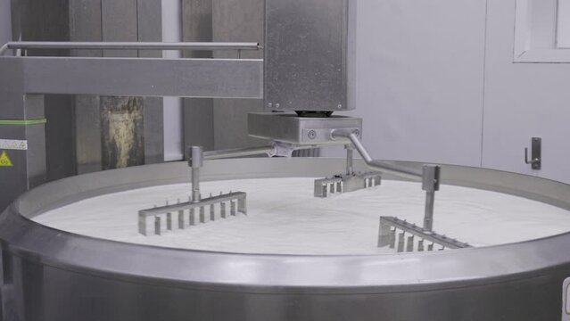 Mechanic arms mixing milk curs in a large industrial size pot at the dairy company