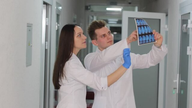 Two young doctors look at the result of a CT scan in the hospital corridor