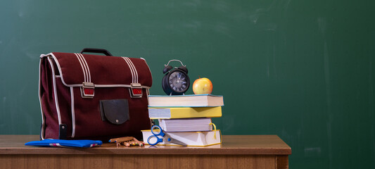 Welcome back to school background - Green blackboard, school bag, textbooks and apple on teacher's...