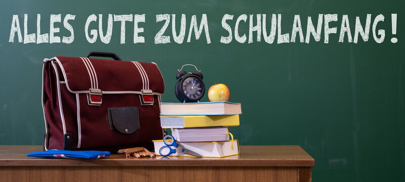 Alles Gute zum Schulanfang Hintergrund Karte mit deutschem Text - Grüne Schultafel, Schulranzen, Schulbücher und Apfel auf Lehrerpult in Klassenzimmer einer Schule