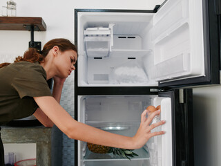 A woman opened the refrigerator and looks sadly into it, wondering what to cook, defrosted the refrigerator, freezer repair in the kitchen at home