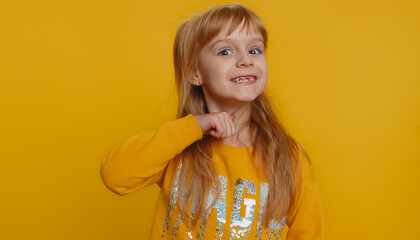 Angry young preteen child girl kid mimicking knife with finger showing gesture of cutting throat. Aggressive little toddler children showing warning sign cut hand neck isolated on yellow background
