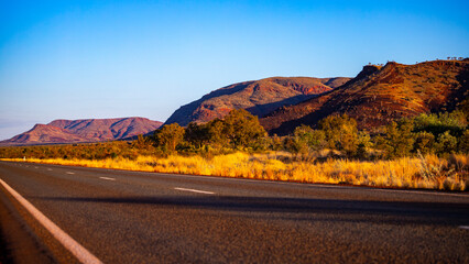sunrise in karijini national park in western australia; a road through the australian outback with red rocks and mountains in the background