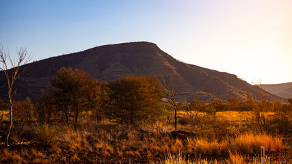 Fototapeta premium Sunrise over mighty mountains in karijini national park in western australia; Australian outback with red rocks, distinctive trees and mountains in the background