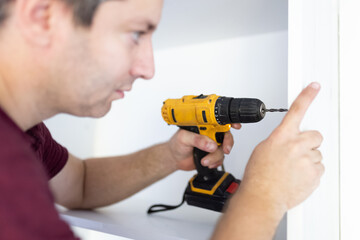 Man assembling white kitchen wooden furniture a home by using cordless screwdriver. Space for copy.