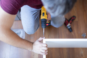 Furniture Installation. Man Using Electric Drill Assembling And Fixing Wooden Shelf Furnishing Room At Home.