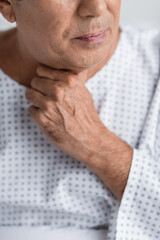 Naklejka premium Cropped view of sick senior man touching neck in hospital.