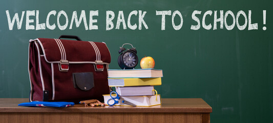 Welcome back to school background - Green blackboard, school bag, textbooks and apple on teacher's...