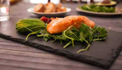 Baked sea trout fillet with fresh vegetables and herbs on black board