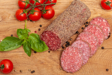 Salami sausage on a wooden board decorated with tomatoes and basil top view