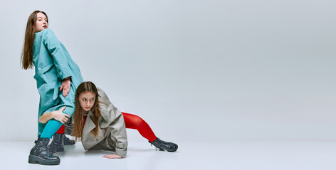Portrait of two young women in bright red and blue tights and coat posing over grey studio...