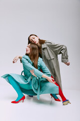 Portrait of two young girls in bright red and blue tights and coat posing over grey studio...