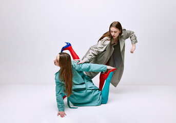 Portrait of two young girls in bright red and blue tights and coat posing over grey studio...