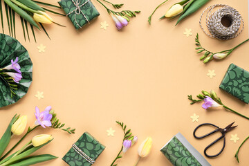 Fototapeta na wymiar Spring freesia and tulip flowers and gift boxes. Golden yellow background with green wrapping paper, scissors and cord. Flat lay, top view with copy-space. Orange, green, purple pastel colors.