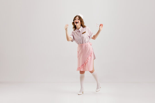 Portrait of young female waitress, sensual woman in retro american fashion style of 70s, 80s in action motion over grey background.