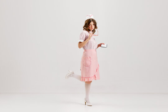 Portrait of young female waitress, sensual woman in retro american fashion style of 70s, 80s in action motion over grey background.