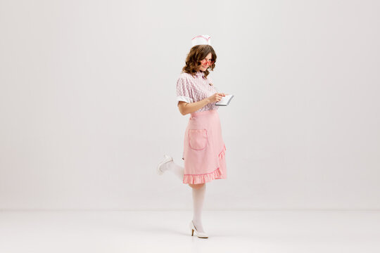 Emotional young woman, retro waitress in american fashion style of 70s, 80s uniform posing over light studio background. Comic photography style