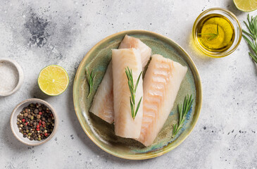 Ceramic plate with fresh cod fish, rosemary, lime, salt and olive oil on gray table. Mediterranean...