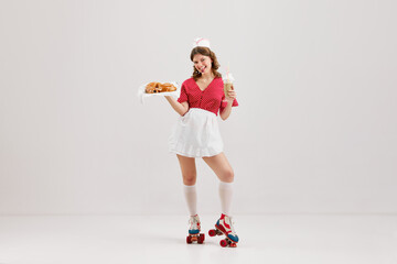 Emotional young woman, retro waitress in american fashion style of 70s, 80s uniform posing over light studio background. Comic photography style - obrazy, fototapety, plakaty