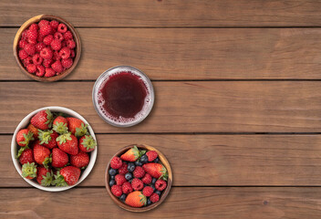 Strawberries, blueberries and raspberries in bowls with juice over wooden table with copy space
