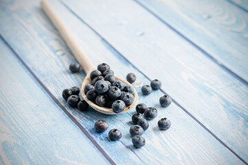 Fresh juicy blueberries with green leaves on a blue background. Healthy berry, organic food, vitamin, blue food.