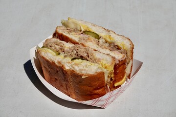 A delicious Cuban sandwich with pulled pork, pickles, cheese and sauce on a paper plate. Authentic...