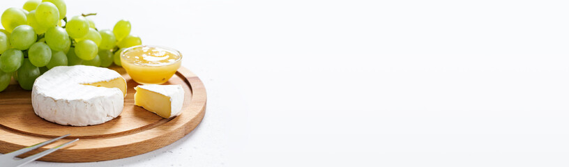 Sliced Camembert with fork on wooden cheese platter on white. Long banner