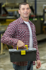 middle-aged engineer carrying a toolbox in a factory