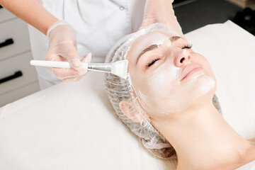 Beautician applies vitamins cream mask on woman face for rehydrate face skin, anti aging cosmetic...