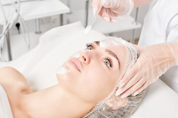 Beautician applies vitamins cream mask on woman face for rehydrate face skin, anti aging cosmetic...