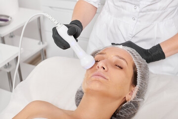 Beautician makes RF lifting for rejuvenation woman face, anti aging cosmetic procedure in beauty spa salon. Cosmetologist makes radio frequency treatment for collagen increasing on female face skin