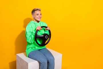 Photo of pretty positive girl sit platform hands hold wheel look empty space isolated on yellow color background