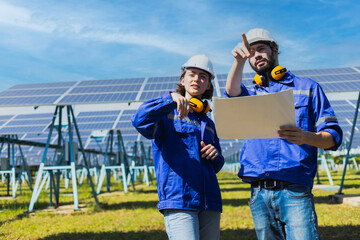 Engineers checking solar panel male and female worker wearing a uniform and safety helmet checking with paper plan on operation of solar panel system at solar station