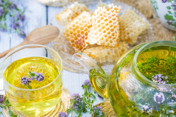 Thyme herbal tea in a glass cup on wicker coaster on wooden table, healthy thyme flower drink with honeycombs in background, healthcare and healthy eating concept