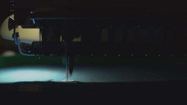 the machine embroiders an inscription on a blue dusty fabric, everything else is in the dark. FullHD high quality video. slow motion video