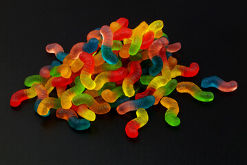 Heap of colorful gummy worms on black background.