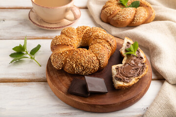 Homemade sweet bun with chocolate cream and cup of coffee on a white wooden. side view.