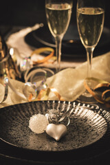 Table setting with decorative heart, two glasses with sparkling wine and party decoration, black and gold colors, vertical