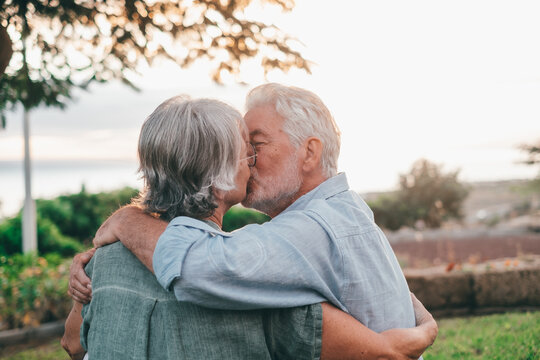 Head shot close up portrait happy grey haired middle aged woman snuggling to smiling older husband, enjoying tender moment at park. Bonding loving old family couple embracing, looking sunset..