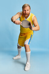 Excited happy man with beard wearing sportswear playing ping-pong isolated over blue background. Concept of active lifestyle, positive emotions, sport