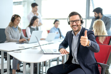 Happy male customer service operator working in call center office and showing thumbs up.