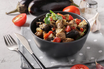 Meat stew with eggplant and tomatoes served in dark bowl on a gray background