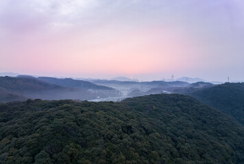Distant early morning sun lights sky pink over misty hilly landscape