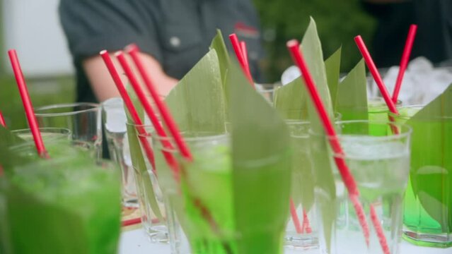 The bartender prepares a lot of cocktails in the catering area on the street. The bartender puts ice in glass glasses, which have a yellow leaf and red tubes. High quality FullHD footage