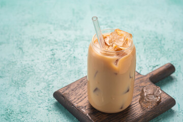 Refreshing drink, Hong Kong style milk tea with ice cubes in a jar-shaped glass cup on a brown...